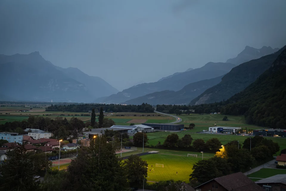 Vue de Vouvry et de la plaine du Rhône au crépuscule, entourées par les montagnes.