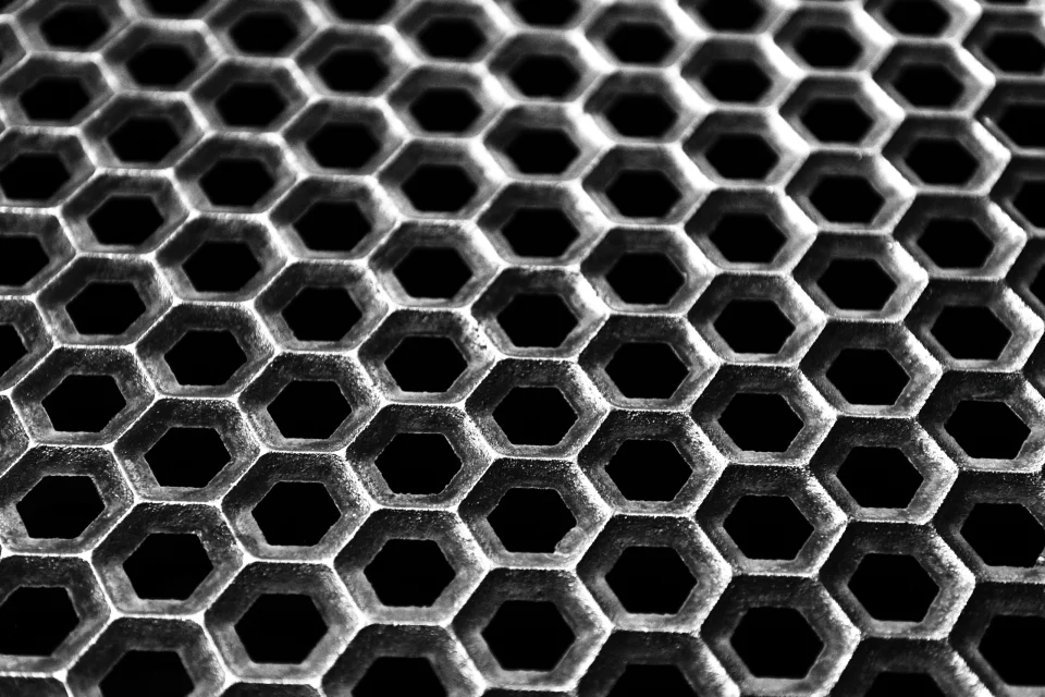 Gros plan en noir et blanc d’une structure composée de nombreuses ouvertures hexagonales éclairées en lumière rasante.